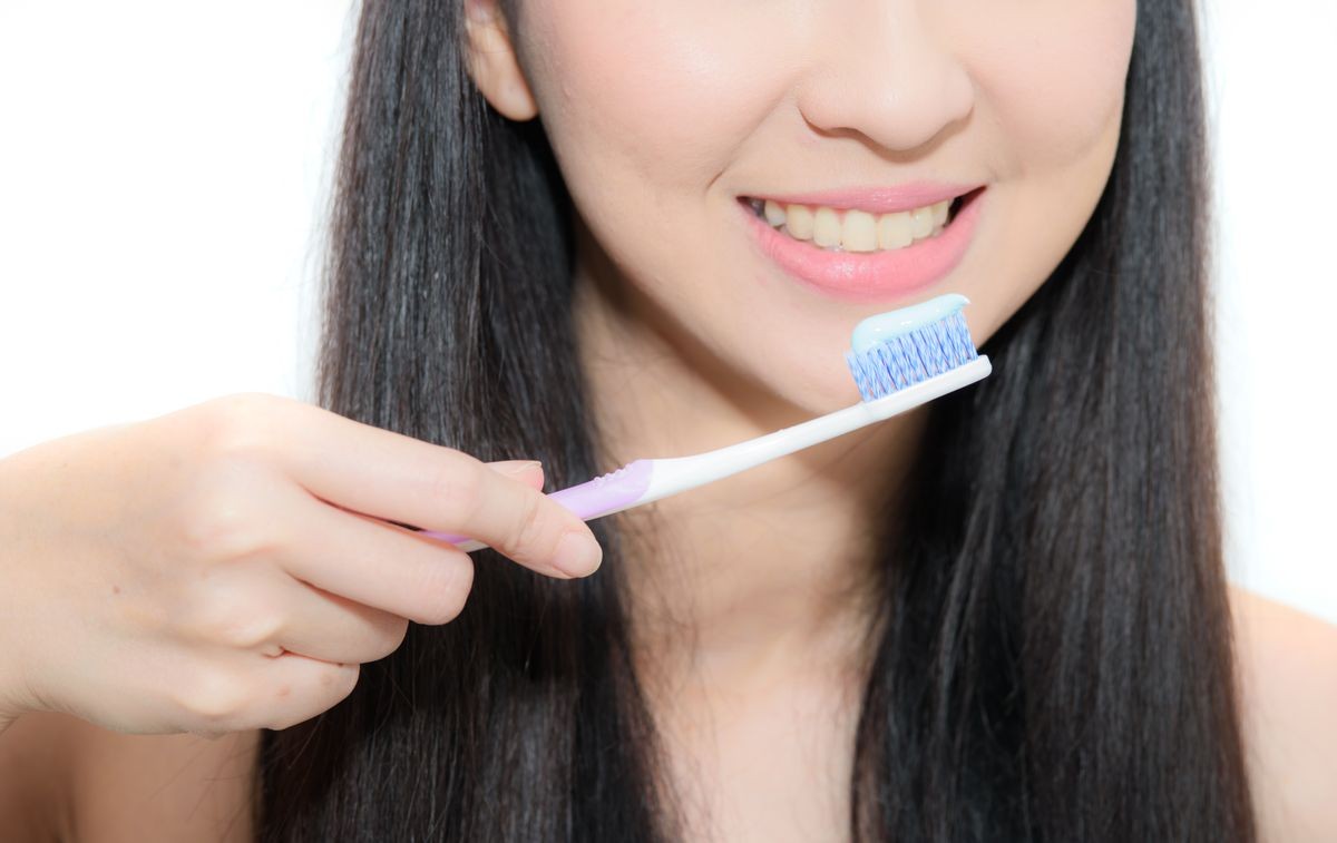Beautiful smiling woman holding a toothbrush and toothpaste, fresh studio portrait on white