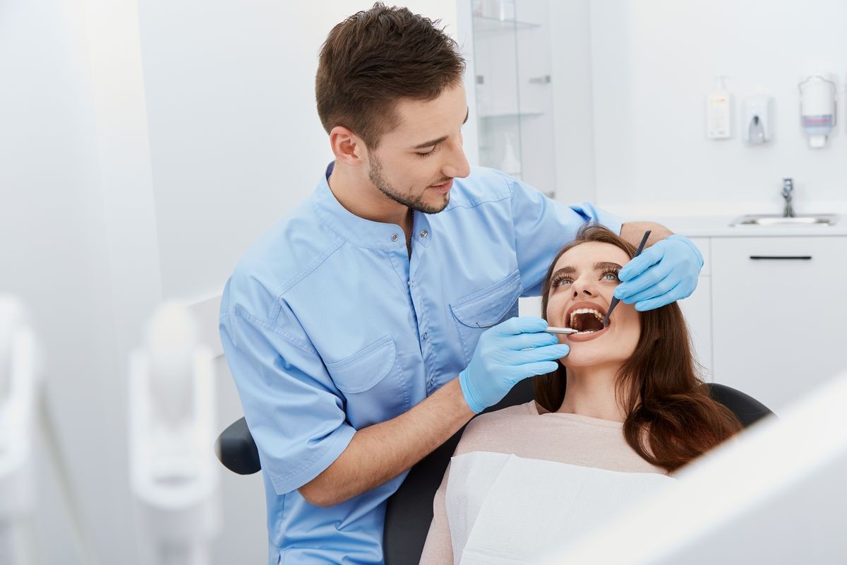 Handsome young dentist working with patient at light medical background, portrait , modern clinic, dental clinic, healthy teeth, satisfied client, close up.